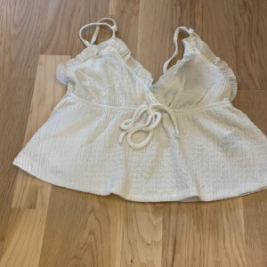 Vit omlottopp med knyt från SHEIN - Supersöt vit omlottopp från SHEIN i storlek XS. Toppen har tunna axelband, v-ringning och knyt i midjan. Materialet är lätt skrynklat och ger en avslappnad känsla. Perfekt för varma dagar och somriga outfits.