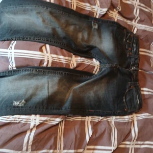 Mörkblå jeans med slitningar 2000stil - Säljer ett par mörkblå jeans med snygga slitningar och flera dekorativa KNAPPAR. Perfekta för dig som gillar en avslappnad och trendig look. SKRIV T MIG HUR LÅNGA NI ÄR ANNARS ÄR DE RISK ATT DOM BLIR FÖRKORTA!
