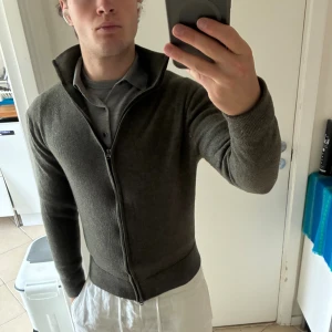 Olivgrön merinoullskofta These Glory Days - Olivgrön kofta från These Glory Days i mjuk merinoull. Modellen har hel dragkedja framtill, hög krage och ribbade muddar. Perfekt för lager-på-lager och snygg till både jeans och chinos. Klassisk och stilren design med normal passform. Helt okej skick, storlek XL men krympt till XS. Koftan sitter bra men lite ”kurvig” längst dragkedjan.