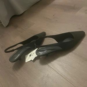 Svarta klackskor  - Svarta klackskor från H&M i storlek 35 med smal klack och spetsig tå. Skorna har öppen häl med rem och är tillverkade i ett tygmaterial med slät finish. ❣️❣️helt oanvända med lappen kvar