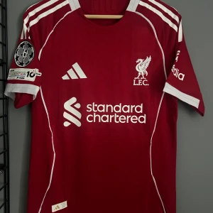 Liverpool röd Adidas matchtröja S - Liverpool FC matchtröja från Adidas i rött med vita detaljer och tryck. Kortärmad modell med klubbmärke, sponsorlogga och Champions League-märke på ärmen. Namn och nummer Wirtz 7 på ryggen. Tillverkad i ventilerande funktionsmaterial. Helt ny tröja. Med tagg . En replika