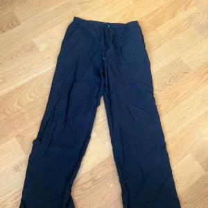 Svarta linnebyxor från Gina Tricot - Svarta linnebyxor från Gina Tricot med avslappnad passform och resår i midjan samt snörning. Byxorna har raka ben och är tillverkade i ett lätt och luftigt linnematerial, perfekta för en chill och stilren look.