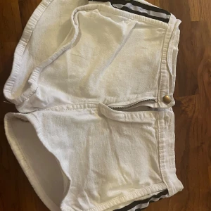 Vita jeansshorts från GBJ, S - Säljer ett par vita jeansshorts från GBJ i storlek S. Shortsen har dragkedja och knapp framtill, två bakfickor och en cool svartvit randig detalj på sidorna. Perfekta för varma dagar och riktigt sköna att bära.