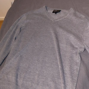 Grå stickad tröja från Lee - Snygg grå stickad tröja från Lee med v-ringad hals och ribbade muddar. Perfekt för lager-på-lager och funkar året runt. Enkel och stilren design som passar till det mesta.