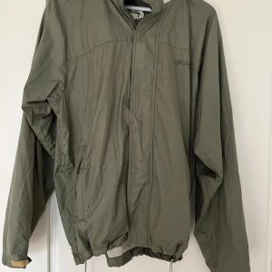 Olivgrön vindjacka från Stüssy M - Vintage vindjacka från Stüssy i storlek M. Jackan har huva, dragsko nertill och meshfoder. Tillverkad i 100% polyester och har Stüssy-logga på bröstet. Luvan kan zippas in i kragen. Tyvärr är dragkedjan sönder och behöver bytas ut hos sömmerska. Därav lägre pris - pris kan även diskuteras! Kan mötas upp på Södermalm. 