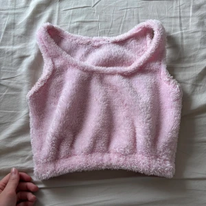 Fluffig ljusrosa ärmlös topp - Supermjuk och fluffig ljusrosa topp med ärmlös design. Toppen har en croppad passform och är tillverkad i ett gosigt fleecematerial som känns som en dröm mot huden. Perfekt för dig som vill ha en mysig och söt look.