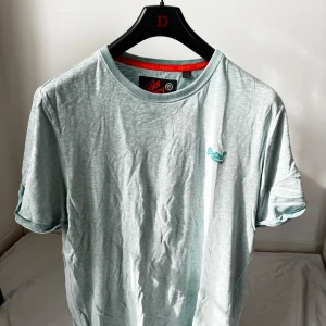 Ljusgrön Superdry t-shirt XL - Fräsch ljusgrön t-shirt från Superdry i storlek XL. T-shirten har rund hals, korta ärmar och ett litet broderat Superdry-logo på bröstet. Tillverkad i mjuk bomull som känns skön mot huden. Perfekt för dig som gillar stilrena och enkla plagg.