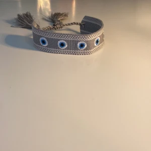 Grå armband med blå ögonmönster som är hemmagjort!!! - Snyggt grått tygarmband med broderade blå ögon längs hela bandet. Jag har gjort det ensam hemma!!! Med lite hjälp från min mamma… Säljer ett för 130kr och två för 180kr!! Skriv för mer frågor!🙂