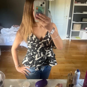 Svartvit omlottopp från Bik Bok - Säljer en svartvit omlottopp från Bik Bok med coolt abstrakt mönster. Toppen har v-ringning, breda axelband och en peplum-liknande volang nertill. Perfekt att styla med jeans eller kjol för en trendig look. Den är lite stor för mig o jag har XS men denna funkar nog som en S.