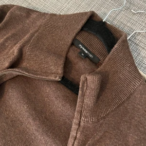 Brun kofta med dragkedja från mywearman - Brun kofta från mywearman i storlek M. Tröjan har ribbad krage och muddar, samt dragkedja framtill. Materialet är mjukt och känns som bomull eller syntet.