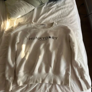 Vit sweatshirt från Hunkydory S - Vit sweatshirt från Hunkydory med svart tryck framtill. Klassisk rund halsringning och långa ärmar. Tillverkad i en mjuk blandning av bomull och polyester för en skön känsla. Perfekt för en avslappnad och stilren look.