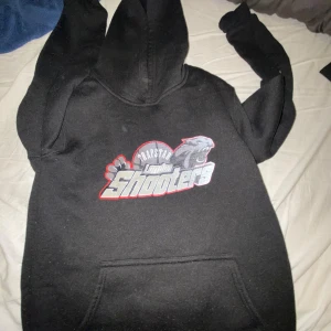 Svarta Trapstar London Shooters mjukisbyxor - Svarta mjukisbyxor från Trapstar med stort tryck av London Shooters och pantermotiv på ena benet. Byxorna har resår i midjan och vid benslut, samt en avslappnad passform. Perfekta för en streetwear-look.