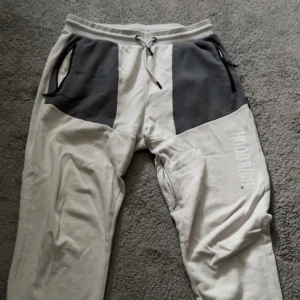 Hoodrich grå mjukisbyxor med tryck - Snygga grå mjukisbyxor från Hoodrich med mörkgrå detaljer vid fickorna, snörning i midjan och tryckt logga längs benet. Baksidan har en ficka med världskarta och Hoodrich-tryck. Perfekta för chill eller streetwear.