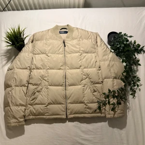 Beige pufferjacka Polo Ralph Lauren M - Snygg beige pufferjacka från Polo Ralph Lauren i storlek M. Jackan har quiltad design, ribbad krage och dragkedja framtill. Perfekt för kyliga dagar med sin stilrena look och bekväma passform. Två snedställda fickor på sidorna och diskret logga i nacken.