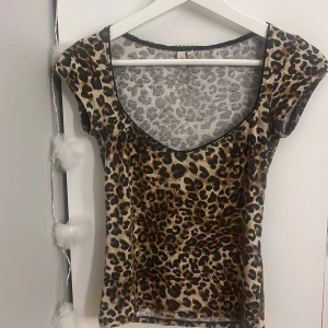 Leopardmönstrad topp från Nelly XS - Säljer en snygg leopardmönstrad topp från Nelly i storlek XS. Toppen har korta ärmar, djup rundringning och svarta spetsdetaljer längs halsringningen. Materialet är stretchigt och följsamt, perfekt för att sticka ut med ett djuriskt mönster.