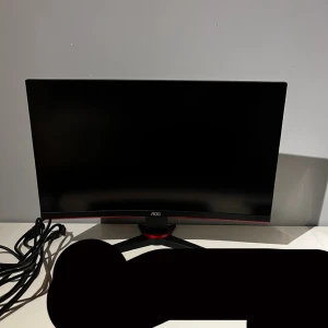 AOC Gaming 240Hz Monitor - AOC Gaming-skärm med 240Hz uppdateringsfrekvens och 1ms responstid, perfekt för snabba spelupplevelser. FreeSync Premium-stöd. Skärmen är i gott skick utan synliga repor eller skador. Medföljer strömkabel. Modern design med röd detalj på foten.
