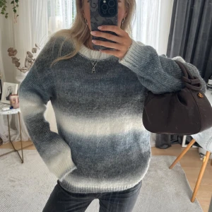 Randig stickad tröja  - Mysig stickad tröja med breda horisontella ränder i grått, blått och vitt. Tröjan har rund halsringning, lång ärm och en loose passform. Perfekt för lager-på-lager och chill dagar. Materialet känns fluffigt och mjukt mot huden.