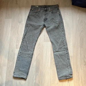 Grå Levi's 501 jeans relaxed fit - Säljer ett par gråa Levi's 501 jeans med klassisk rak passform och fem fickor. Jeansen har hög midja, knappgylf och den ikoniska läderpatchen bak. Materialet är robust denim i bomull och färgen är snyggt tvättad grå. Perfekta för en avslappnad och tidlös look. Små slitningar i hälsömmarna. Säljer då jag inte använder dem längre