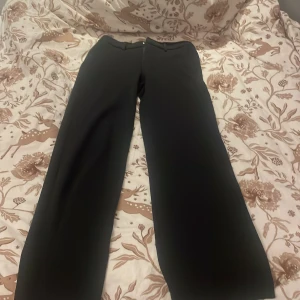 Svarta kostymbyxor med raka ben - Snygga svarta kostymbyxor med raka, lite vidare ben och klassisk passform. Byxorna har hällor för bälte, dold dragkedja och metallknapp i midjan. Perfekta för en clean och stilren look. Materialet känns mjukt och följsamt.