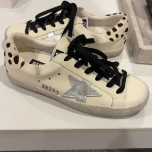 GoIden goose sneakers  - Snygga goIden goose vita sneakers med svarta snören, silverfärgad stjärna på sidan och coola polcka dots på baksidan av skon. Skorna har en platt sula och är tillverkade i skinn. Perfekta för dig som vill sticka ut med en unik och trendig look. 💓🩷