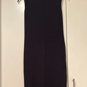 Svart ribbad långklänning från Neohit - Säljer en svart långklänning från Neohit i ribbad bomullsmix. Klänningen har en tight passform och ett coolt cut out-detalj vid axeln som ger en trendig look. Perfekt för dig som gillar minimalistisk stil och vill ha något enkelt men snyggt.