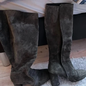 Grå mockastövlar med klack - Snygga höga stövlar i mörkgrå mocka med bred klack och dragkedja på insidan. Perfekta för att lyfta din outfit med en trendig touch. Stövlarna har en klassisk form och passar till många olika stilar.