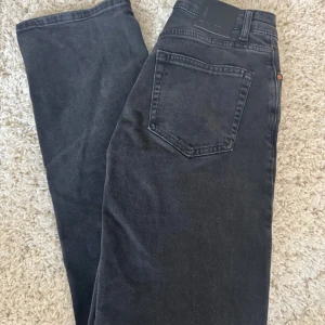 Svarta wide jeans från Gina Tricot - Snygga svarta jeans från Gina Tricot i modellen Mid Wide. Jeansen har medelhög midja, raka vida ben och klassisk femficksdesign. Tillverkade i mjuk denim med knapp och dragkedja framtill. Perfekta för en trendig och avslappnad look.