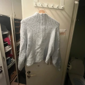 Ljusblå stickad tröja från Weekday - Mysig ljusblå stickad tröja från Weekday med half zip framtill och hög krage. Tröjan har långärmade ärmar och en ribbad detalj upptill som ger extra stil. Perfekt för kyliga dagar och enkel att matcha med jeans eller kjol.