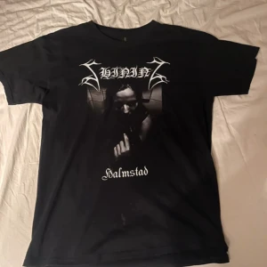 Shining Halmstad band t-shirt svart - Black metal band t-shirt från Shining med tryck av albumet Halmstad på bröstet. Storlek L normal i storleken. Lätt missfärgning på ärmen men inga andra defekter.  Lätt material.