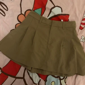 Beige kortkjol i bomull - Säljer en beige kortkjol med klassisk A-linjeform och bälteshällor i midjan. Kjolen är sydd i ett stadigt bomullstyg och har en enkel, stilren look som är lätt att matcha med olika toppar och jackor.