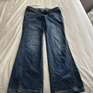LEVI’S NOUGHTIES BOOTCUT WOMEN'S JEANS  - Blå jeans från Levi's med bootcut passform och rå,. Klassiska bakfickor med lock och silverfärgade knappar, samt brunt läderpatch bak i midjan. Snygga kontrastsömmar.	Klassisk low-rise bootcut-passform, lite slitet längst ner, använt bara några gånger, säljer dessa jeans för de är för små för mig  	•	Äkta 2000-talsinspirerad design 	•	Grova sömmar + Y2K-fickdetaljer 	•	Tillverkade i TENCEL™ Lyocell för mjukhet och hållbarhet. Även Slutsålt på hemsidan 
