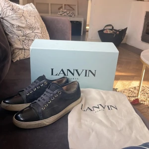 Lanvin skor - Snygga svarta sneakers från Lanvin med ovandel i mocka och lackad tå. Skorna har vita sulor och klassisk snörning med metallöljetter. Perfekta för dig som gillar stilrena och exklusiva sneakers med en twist.