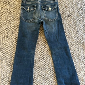 Blå bootcut jeans från Gina Tricot - Såå snygga blå jeans från Gina Tricot i storlek 158. Modellen har bootcut-ben, klassiska fickor med lock och silverfärgade knappar bak. Jeansen har ljusa slitningar och kontrastsömmar för en cool look. Perfekta för dig som gillar en avslappnad stil💕