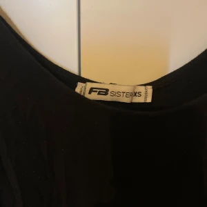 Svart linnetopp från FB Sister XS - Svart linnetopp från FB Sister i storlek XS. Toppen har breda axelband och en rundad halsringning. Den är lätt utsvängd nertill och passar perfekt till jeans eller kjol. Enkel och stilren design som funkar till många olika looks.