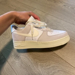 Nike Air Force 1 i ljusbeige och vitt - Säljer ett par Nike Air Force 1 i en clean ljusbeige och vit färg. Skorna har klassisk låg siluett, snörning och platt sula. Ovandelen är i en mix av skinn och mocka för en snygg kontrast. Perfekta för dig som gillar stilrena sneakers med ikonisk design.