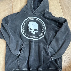 Number (N)ine hoodie - Cool svart hoodie från Number (N)ine med stort döskalletryck och text på bröstet. Tröjan har huva, magficka och en avslappnad passform. Perfekt för dig som gillar streetwear och vill sticka ut med en unik look.