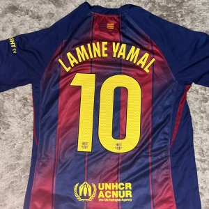 FC Barcelona Lamine Yamal #10 Nike tröja M - Säljer en officiell FC Barcelona matchtröja från Nike med Lamine Yamal och nummer 10 på ryggen. Tröjan är kortärmad, har klassiska blå och röda ränder, gula detaljer och klubbmärke på bröstet. Tillverkad i Dri-FIT material för bästa komfort. Perfekt för alla Barca-fans!
