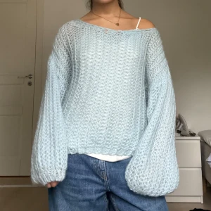 Alpacka-blend Ljusblå stickad tröja från Noella - Superfin ljusblå stickad tröja från Noella med oversized passform och ballongärmar. Tröjan har en lös, luftig struktur och bred halsringning som kan bäras offshoulder. Perfekt att styla med jeans för en chill look.