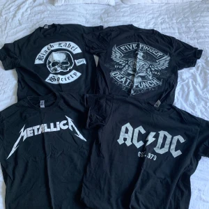 Svarta band-tshirts Metallica AC/DC m.fl. - Fyra svarta band-tshirts med tryck från Metallica, AC/DC, Black Label Society och Five Finger Death Punch. Klassiska kortärmade modeller i bomull med stora vita loggor och motiv på bröstet. Perfekta för dig som gillar rock och metal. Storlek M