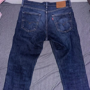 Levi's 501 mörkblå jeans - Klassiska Levi's 501 jeans i mörkblå tvätt med raka ben och femficksmodell. Jeansen har snygga kontrastsömmar, läderpatch bak i midjan och den ikoniska röda Levi's-taggen på bakfickan. Perfekta för dig som gillar en tidlös och avslappnad look.