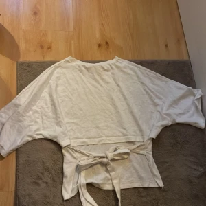 Vit omlottopp med knyt från Nelly - Säljer en vit omlottopp från Nelly i storlek S. Toppen har vida ärmar, rund halsringning och knytband vid ryggen som ger en snygg siluett. Perfekt för dig som gillar en enkel men trendig look.
