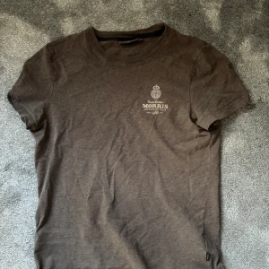 Brun t-shirt från Morris XS - Säljer en brun t-shirt från Morris i storlek XS. T-shirten har rund halsringning, korta ärmar och en liten tryckt logga på bröstet. Skön passform och tillverkad i mjuk bomull. Perfekt för en clean och stilren look. Skicket är 9/10 använd fåtal gånger.