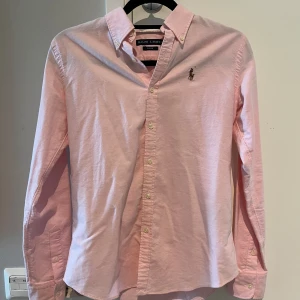 Ralph Lauren skjorta  - Säljer en ljusrosa skjorta från Ralph Lauren i slim fit-modell. Storlek 2 men jag skulle säga att den motsvarar en större XS, mindre S. Använd endast 1-2 gånger då den inte passar mig. Skick 9/10. Nypris: 1995kr. 