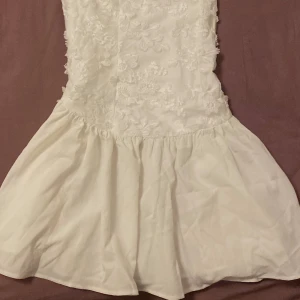 Vit kort klänning med blommor - Vit kort klänning perfekt för studenten och andra tillfällen. Passar S/M. Aldrig använd, helt ny. 