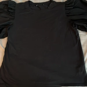 Svart topp med puffärmar - Säljer en svart topp med coola puffärmar som ger en trendig siluett. Toppen har rund halsringning och är tillverkad i mjukt material, perfekt för dig som vill sticka ut lite extra. Passar till både jeans och kjol för en snygg look.