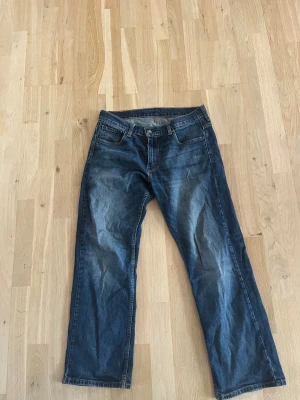 Levi's 569 blå jeans W30 L30 - Säljer ett par klassiska Levi's 569 jeans i mörkblå tvätt med snygga slitningar. Modellen har rak passform och breda ben, fem fickor och tydliga kontrastsömmar. Perfekt för dig som gillar en avslappnad och stilren look.