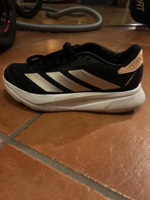 Adidas Duramo SL2 svarta sneakers - Adidas Duramo SL2 sneakers i svart med silvriga/beige ränder och beige/rosa detaljer vid hälen. Skorna har snörning, Outdoor-innersula och en tjock vit platt sula. Ovandelen är i mesh och syntet, vilket ger bra ventilation och komfort. Perfekta för träning eller en aktiv vardag. Använda fåtal ggr😃🙌