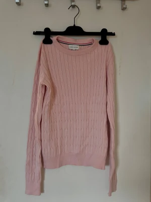 Ljusrosa stickad tröja från Panos Emporio - Supersöt ljusrosa stickad tröja från Panos Emporio med klassiskt kabelstickat mönster. Rund halsringning och långa ärmar ger en chill och clean look. Perfekt att matcha med jeans eller kjol för en soft stil. Storlek 158/164 men passar lätt en S/Xs