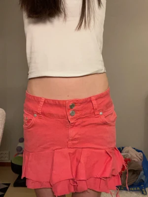 Rosa volangkjol från LTB Jeans - Supersöt rosa kortkjol från LTB Jeans med volangdetaljer och råa kanter. Kjolen har klassisk jeanslook med fickor fram och bak, dubbla knappar i midjan och en cool, avslappnad vibe. Perfekt för dig som vill sticka ut med en färgglad och lekfull stil. Tyvärr sydd där bak då den var för stor på mig men borde gå att ta bort. Mycket trådar kan synas men handgjord och köpt på Vinted. Själv ca 152cm och den är ganska lång på mig.