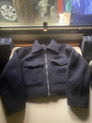 Marin blå  teddyjacka från Zara XS - Säljer en marin blå  teddyjacka från Zara i storlek XS. Jackan har en croppad passform, två stora fickor framtill och dragkedja. Materialet är fluffigt och ger en cool vibe, perfekt för dig som gillar streetstyle. Klassisk krage och långärmad modell.
